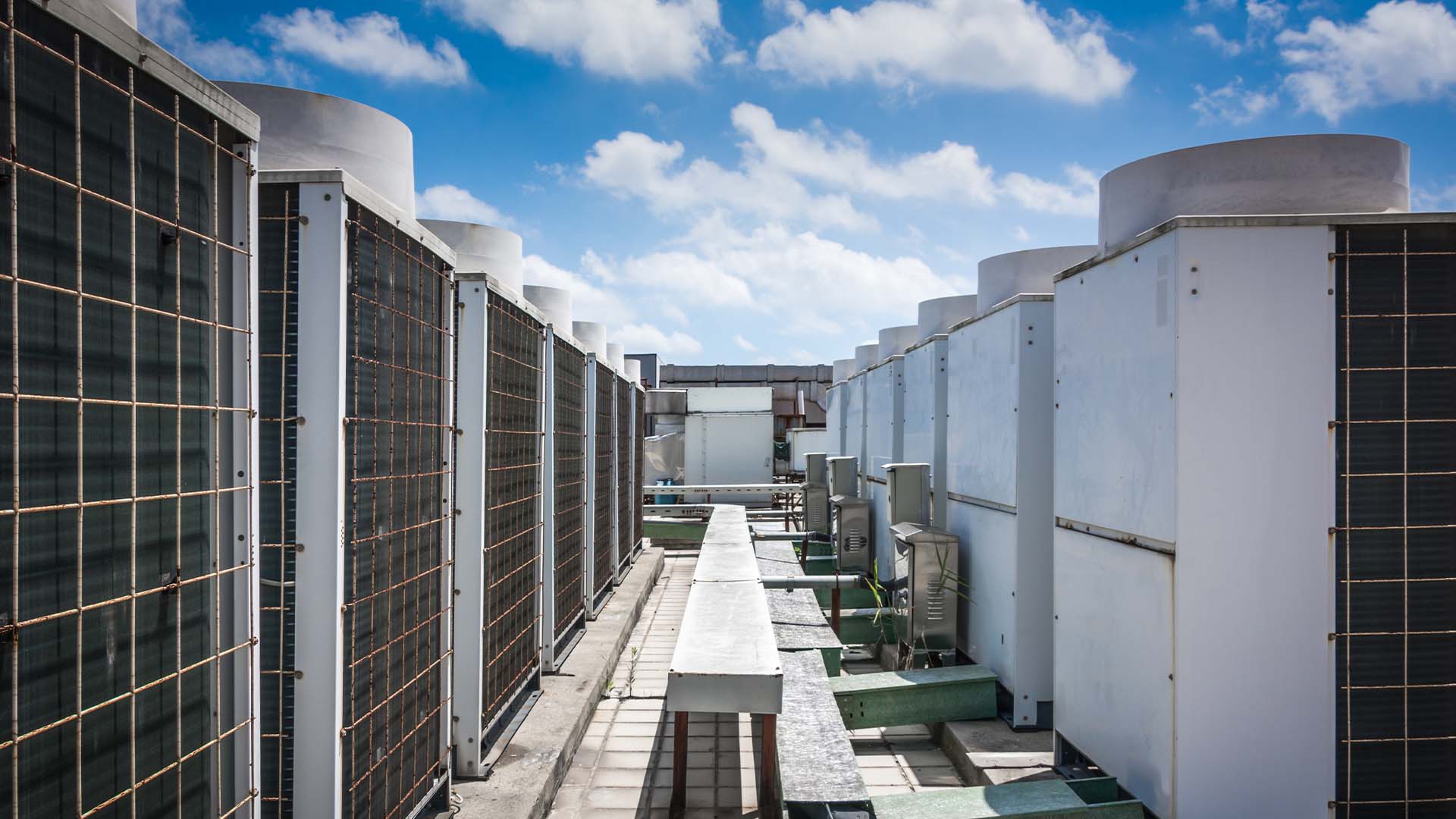 A row of rooftop air conditioning units sit atop a roof