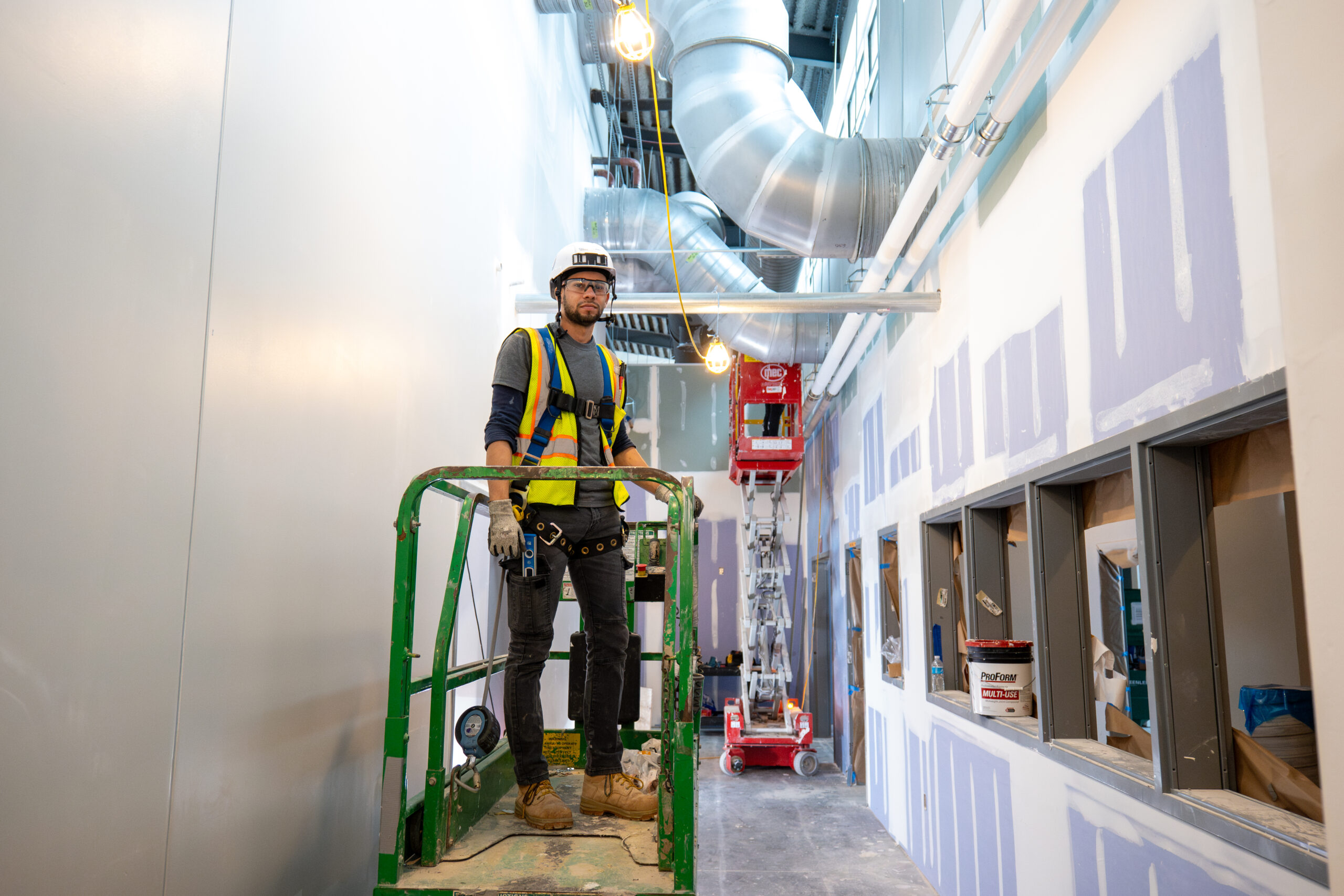 Superintendent standing on scissor lift in busy construction job site.