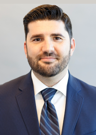 Professional headshot of a man wearing a navy blue suit and striped tie against a light gray background.